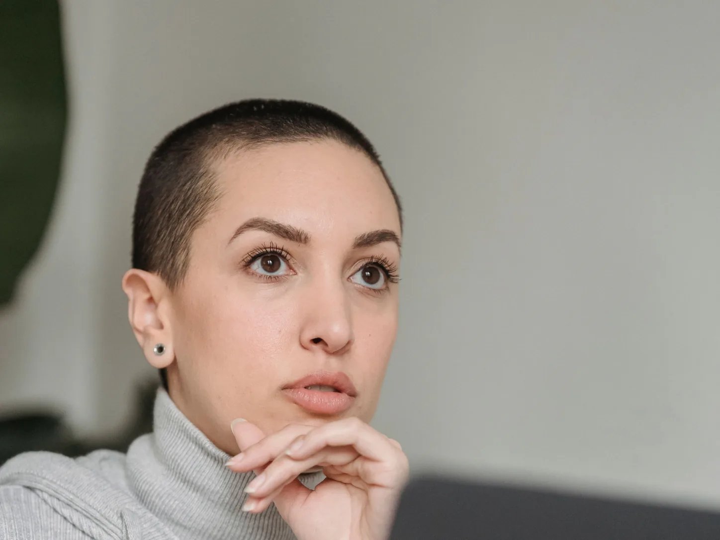 Zamyślona osoba przy laptopie, z dłonią opartą o brodę