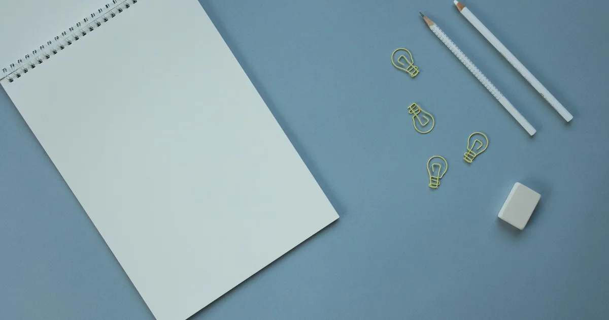 Pusty notes obok ołówków, gumki i spinaczy w kształcie żarówek